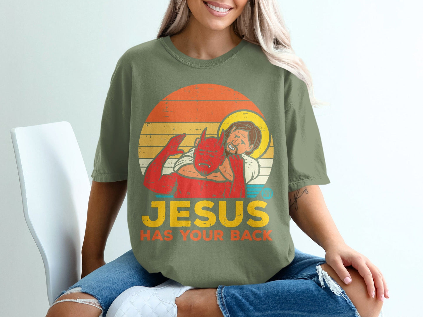 T-shirt with devil hugging Jesus, text reads "Jesus Has Your Back".