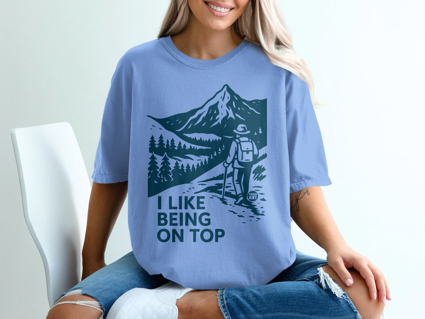 Blue t-shirt with graphic of a hiker on a mountain path with text "I like being on top".