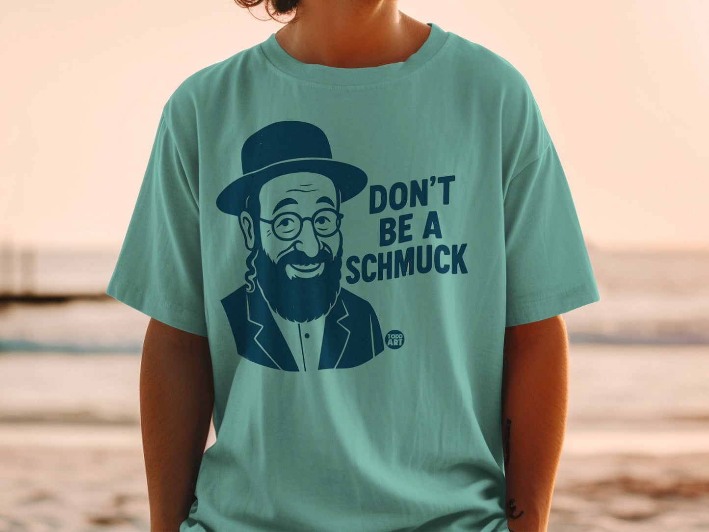 Teal t-shirt with a drawing of a man in a hat and glasses, and text "DON'T BE A SCHMUCK".