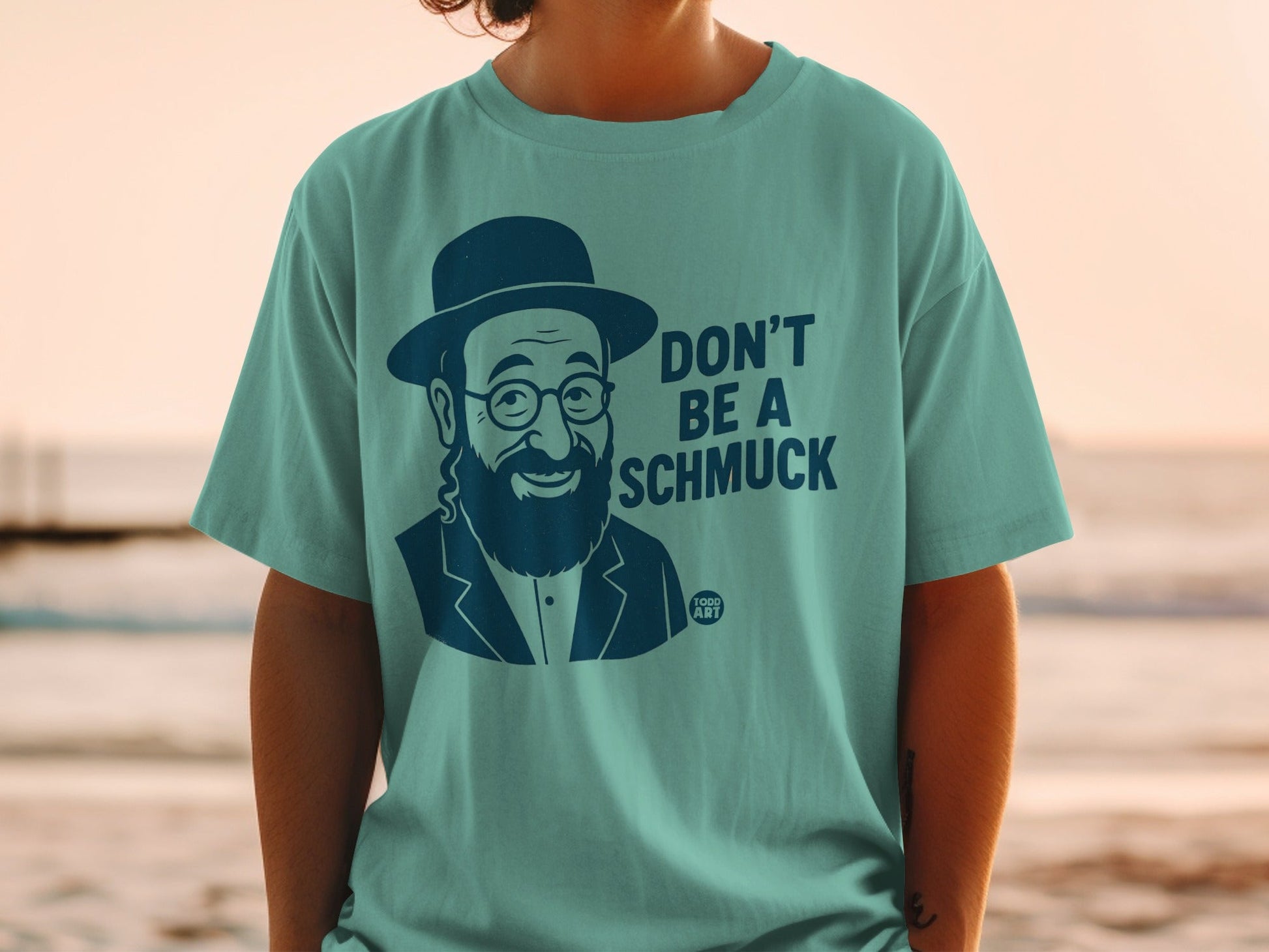 Teal t-shirt with a drawing of a man in a hat and glasses, and text "DON'T BE A SCHMUCK".