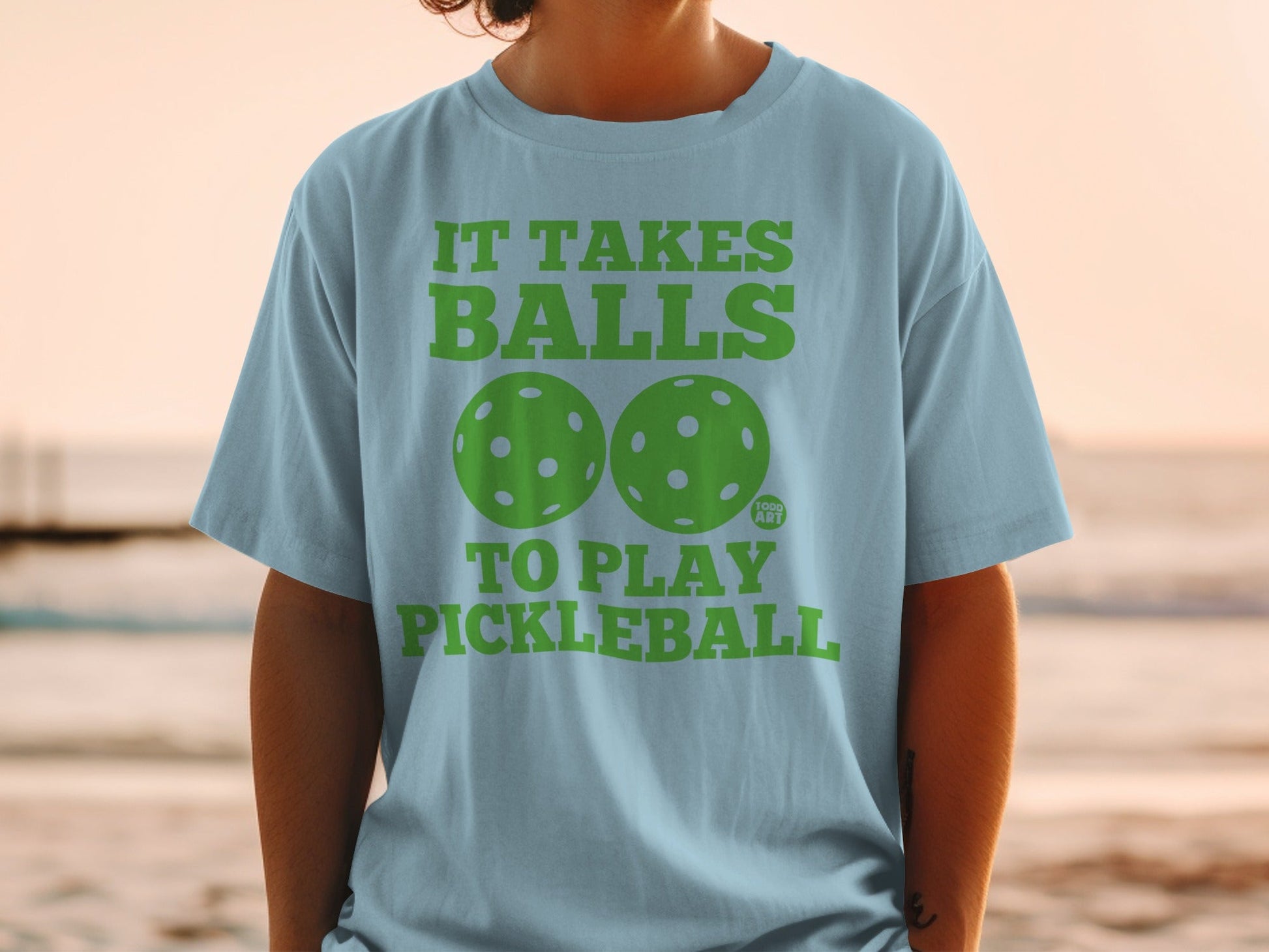 Light blue t-shirt with "IT TAKES BALLS TO PLAY PICKLEBALL" and two pickleballs.