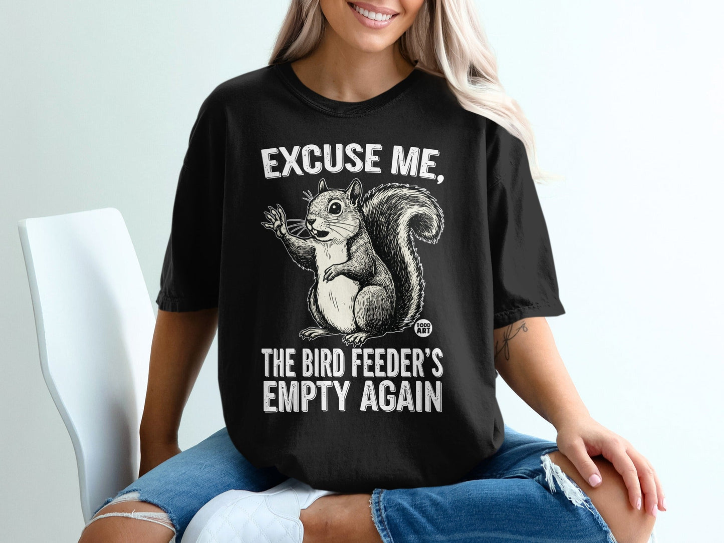 Black t-shirt with a cartoon squirrel and text: "EXCUSE ME, THE BIRD FEEDER'S EMPTY AGAIN."