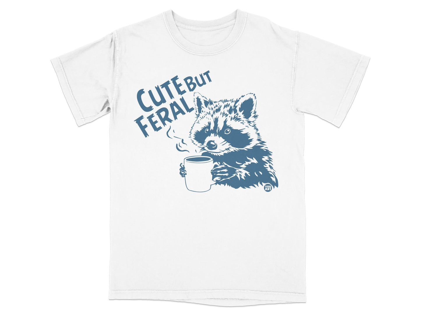 White t-shirt with blue raccoon holding coffee mug, text "CUTE BUT FERAL".