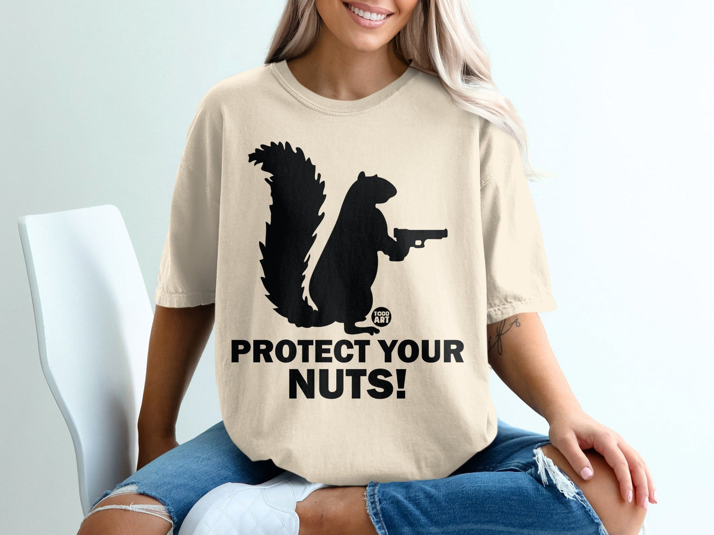 Cream t-shirt with a black squirrel holding a gun and text "PROTECT YOUR NUTS!".