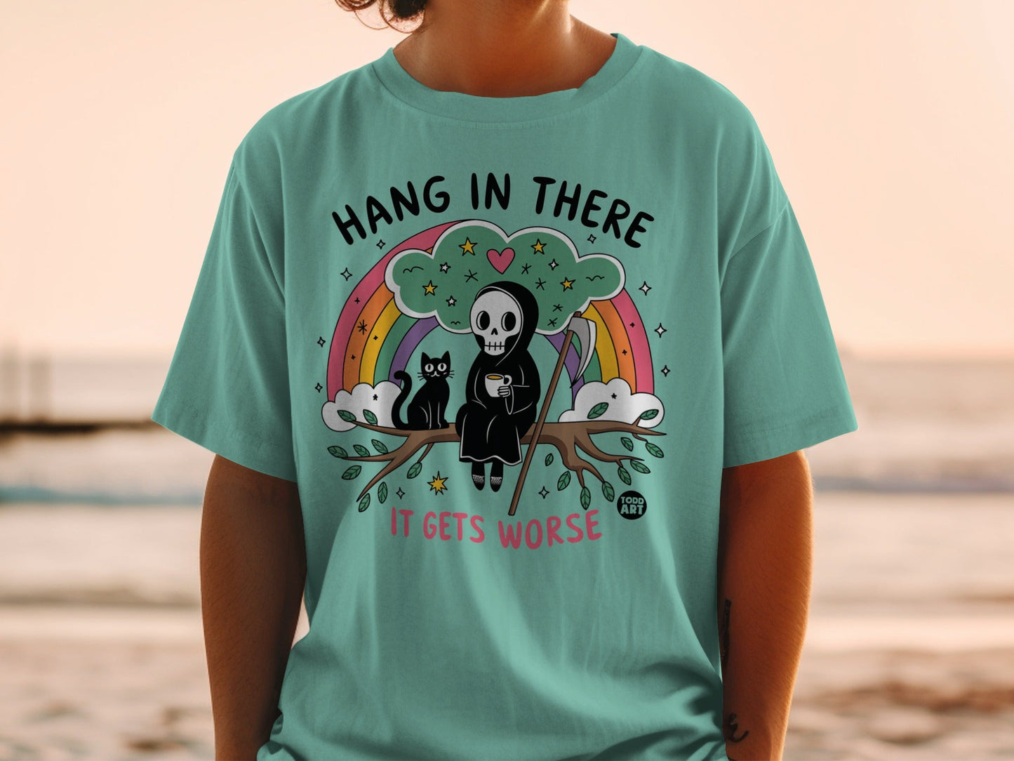 Teal t-shirt with Grim Reaper and cat on rainbow, "Hang in there it gets worse" text.