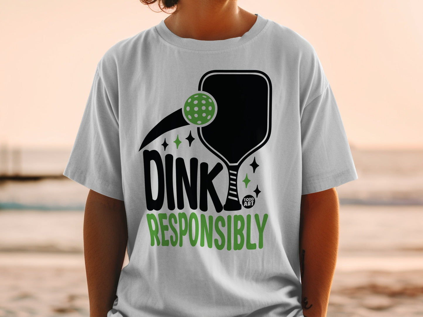 White t-shirt with black pickleball paddle and "DINK RESPONSIBLY" text.