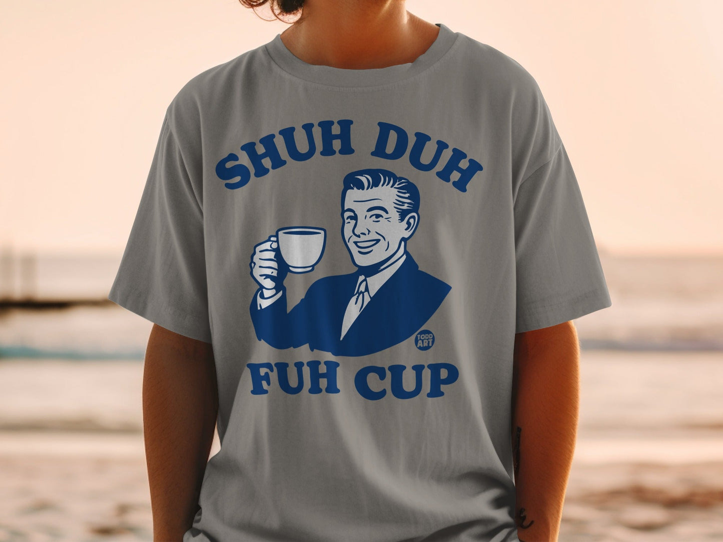 Grey t-shirt with "SHUH DUH FUH CUP" and smiling man holding mug.