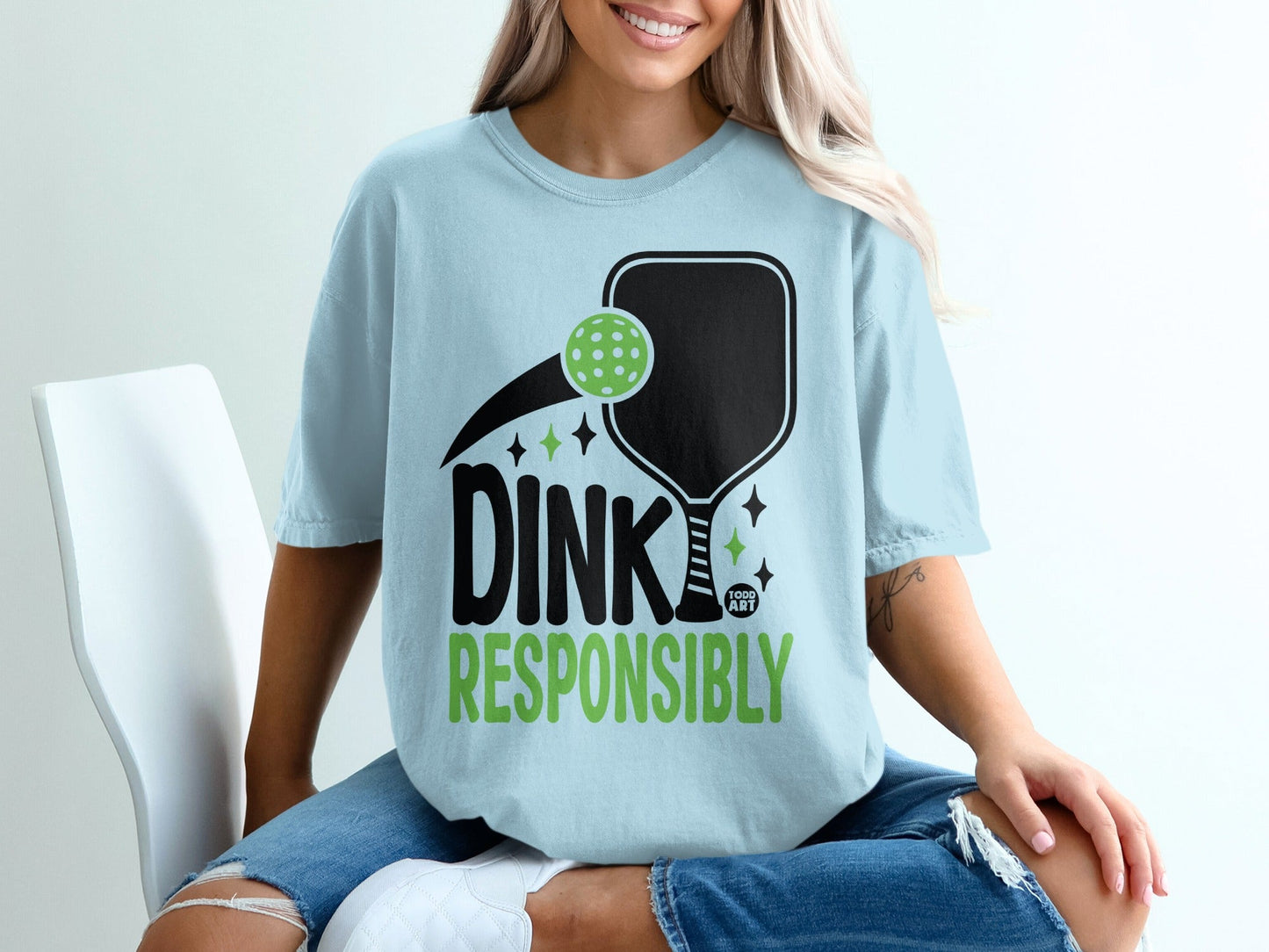 Light blue t-shirt with "DINK RESPONSIBLY" text, pickleball paddle, and balls.