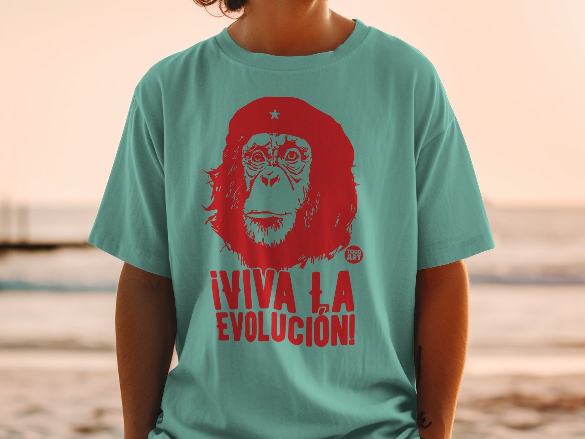 Red primate graphic with ¬°VIVA LA EVOLUCI√ìN! text on teal t-shirt.