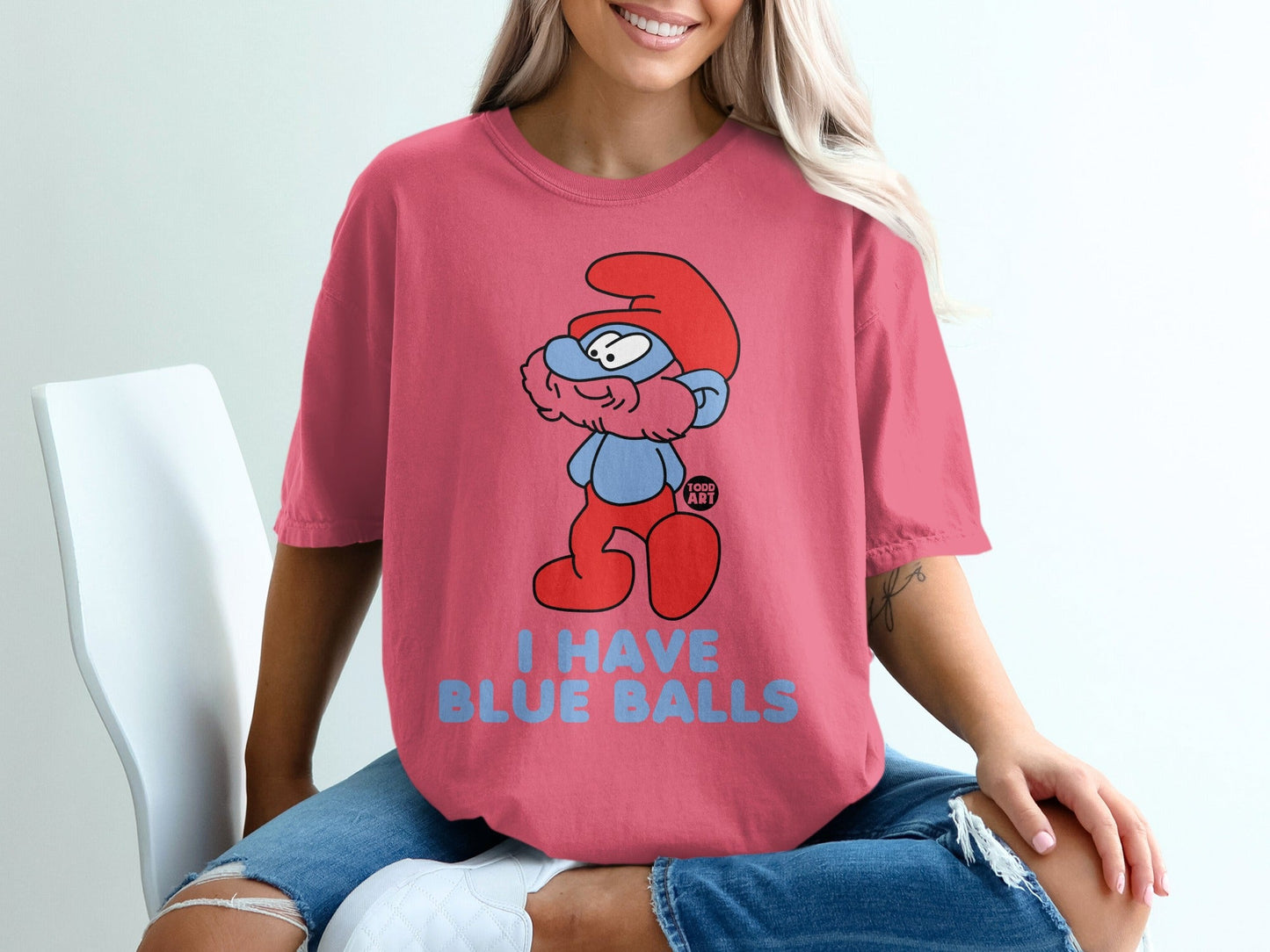 Smurf with red hat and blue shirt, text "I HAVE BLUE BALLS" on pink t-shirt.