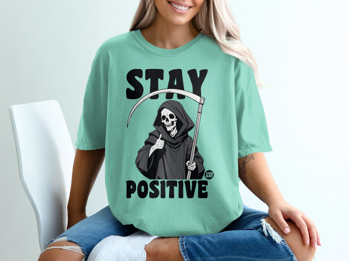 Teal t-shirt with Grim Reaper giving thumbs up and "STAY POSITIVE" text.