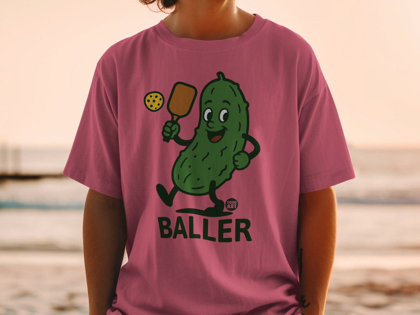 Cartoon pickle playing pickleball, wearing a pink t-shirt.