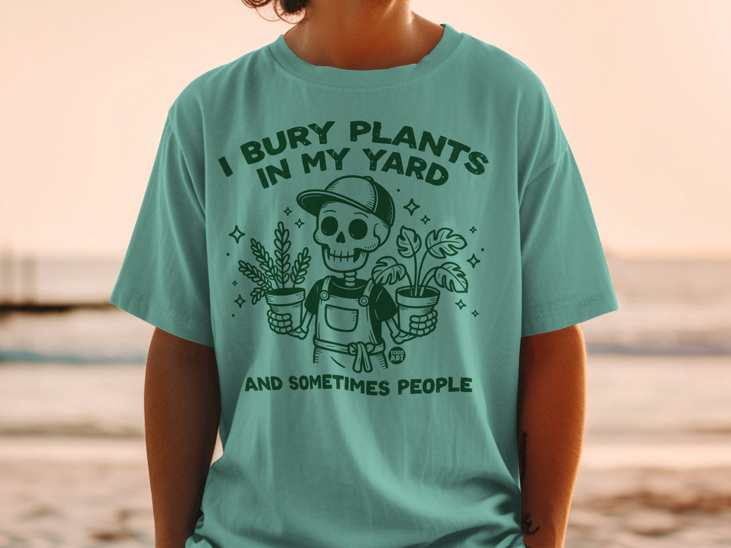 Teal t-shirt with a skeleton planting, "I bury plants in my yard and sometimes people."
