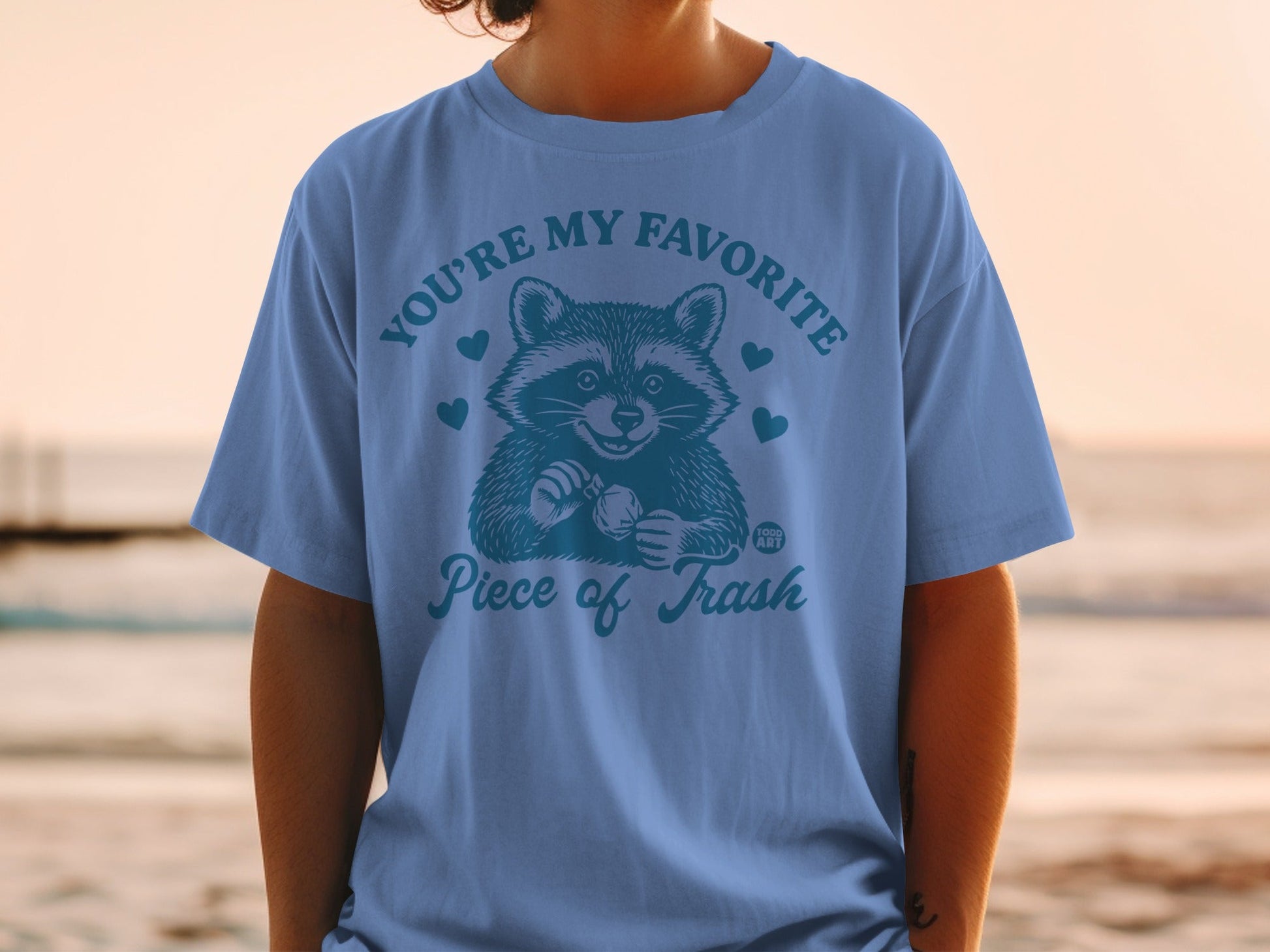 Blue t-shirt with raccoon graphic and "YOU'RE MY FAVORITE Piece of Trash" text.