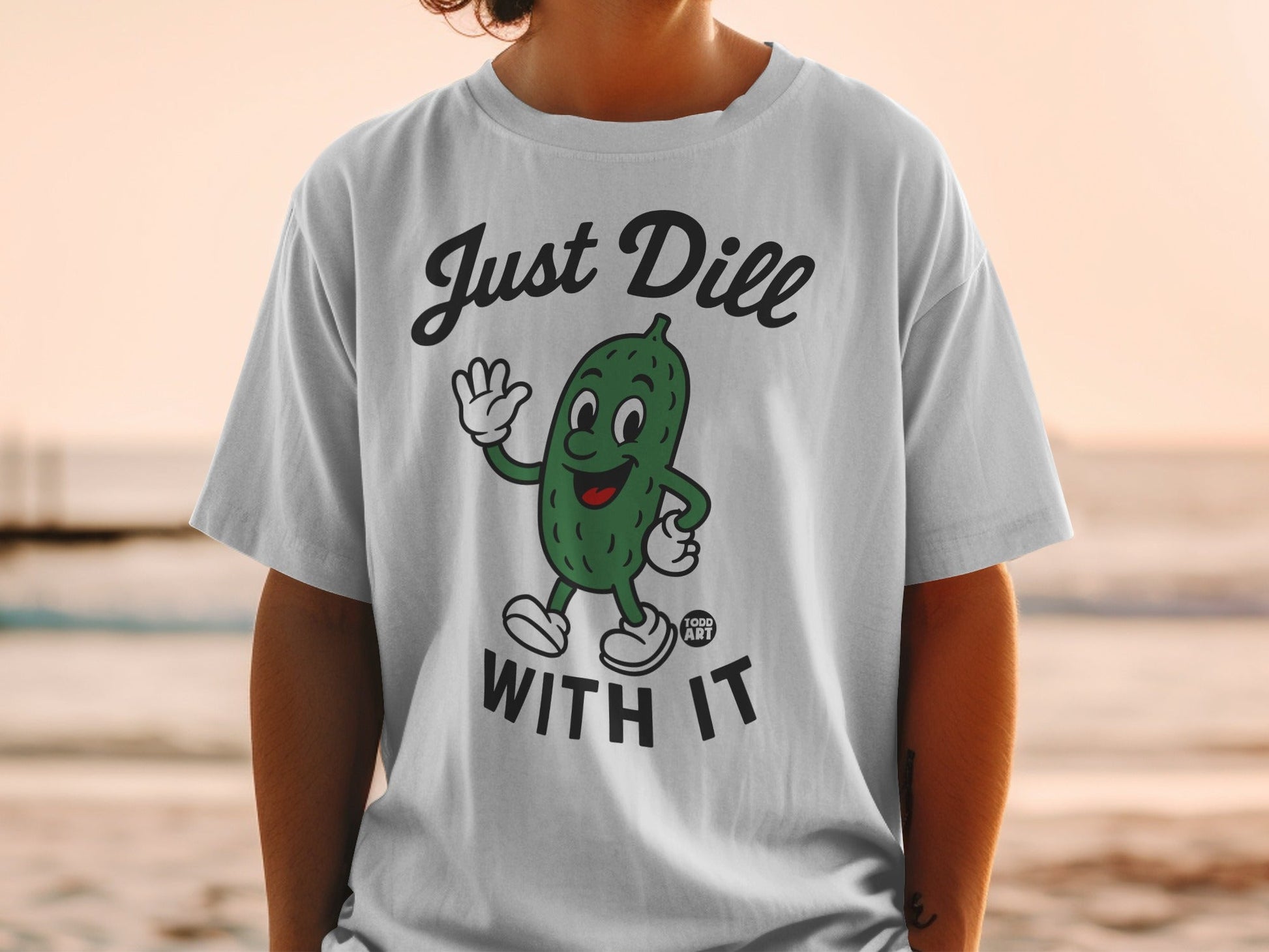 White t-shirt with cartoon pickle saying "Just Dill With It".