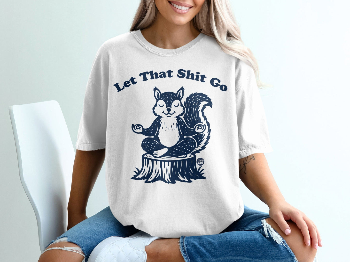 White t-shirt with a meditating squirrel on a stump and "Let That Shit Go" text.