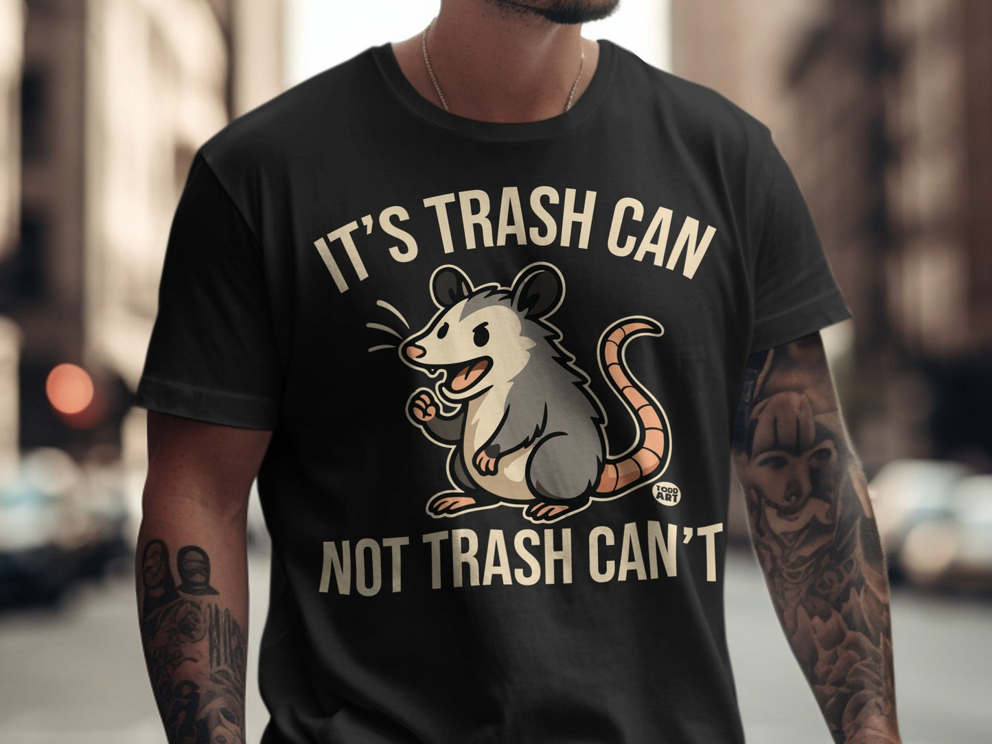 Black t-shirt with a cartoon opossum and text "It's trash can, not trash can't".