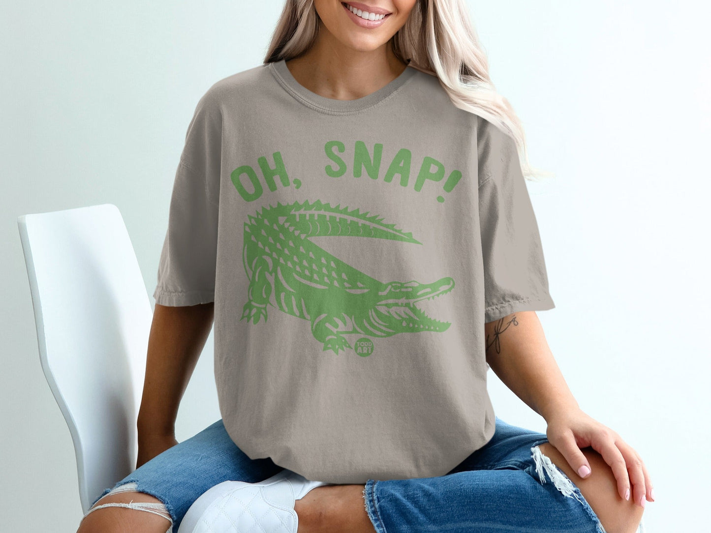 Green alligator graphic with "OH, SNAP!" text on a tan t-shirt.