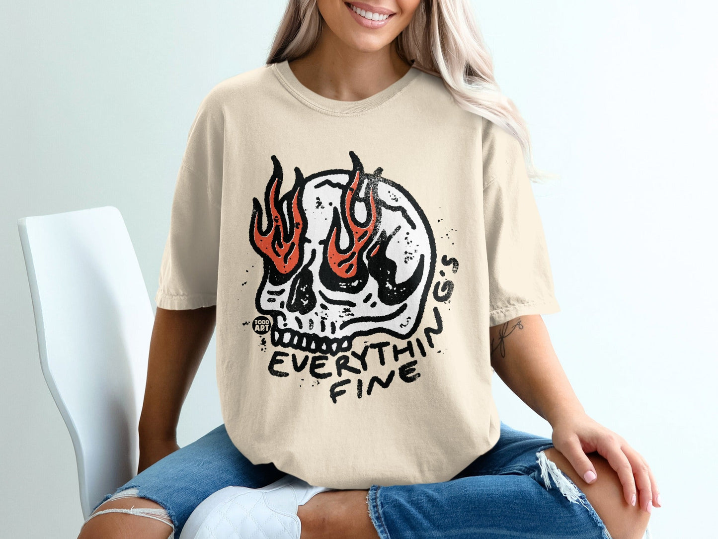 Cream t-shirt with a black skull graphic engulfed in flames and "EVERYTHIN FINE" text.