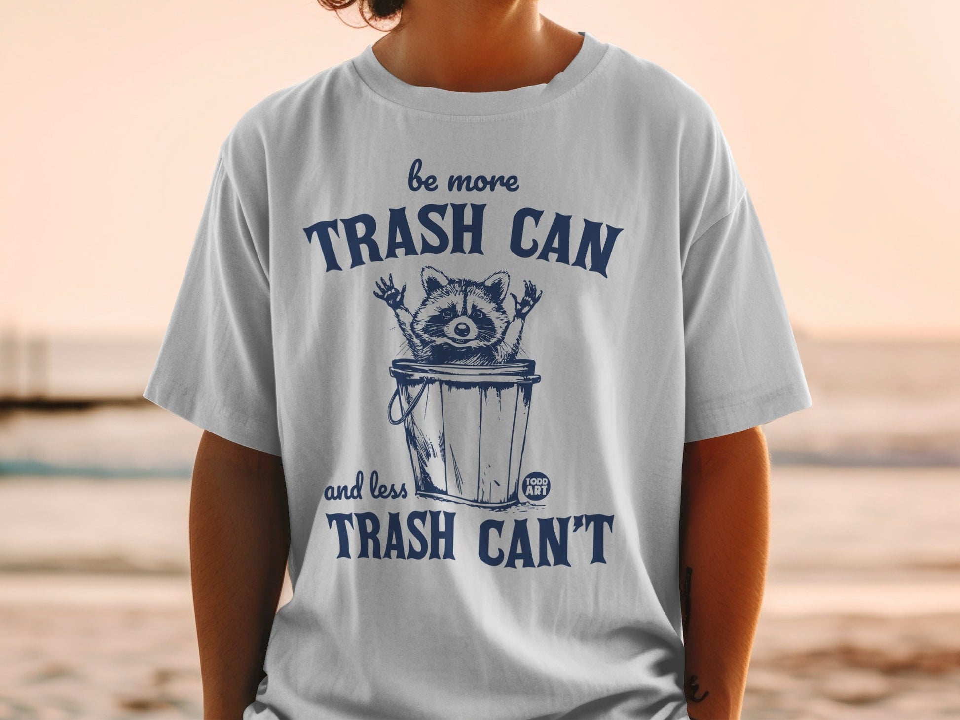 T-shirt with raccoon in trash can graphic and text "be more TRASH CAN and less TRASH CAN'T".