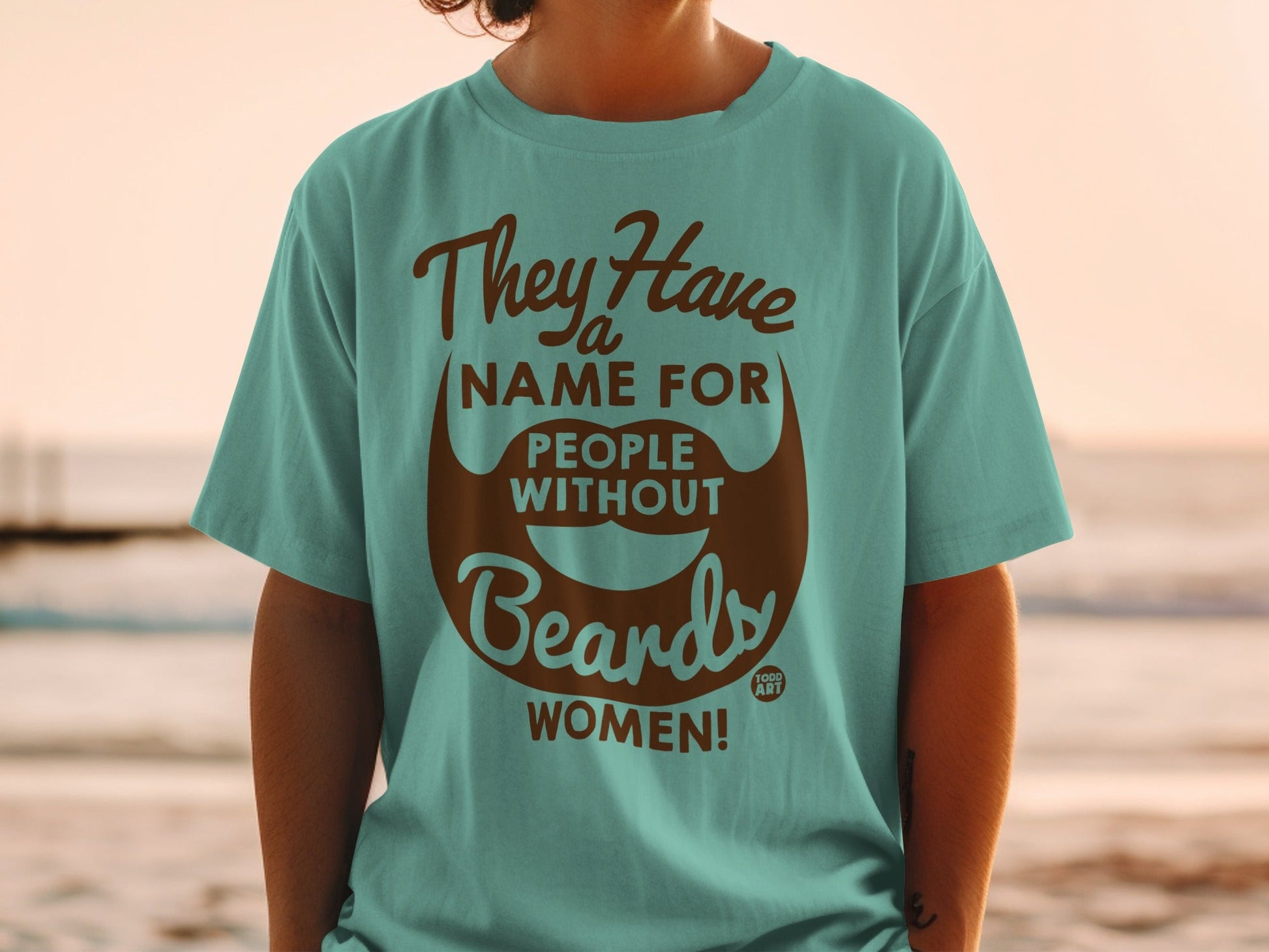 Teal t-shirt with brown text and a beard graphic saying "They Have a Name For People Without Beards: WOMEN!"