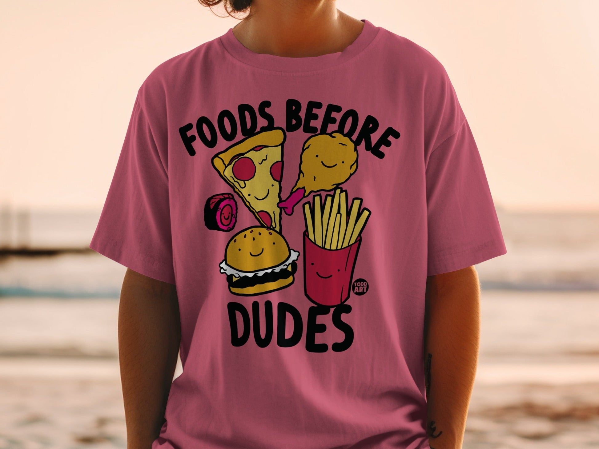 Pink t-shirt with cartoon pizza, burger, chicken, fries, and sushi, reading "Foods Before Dudes".