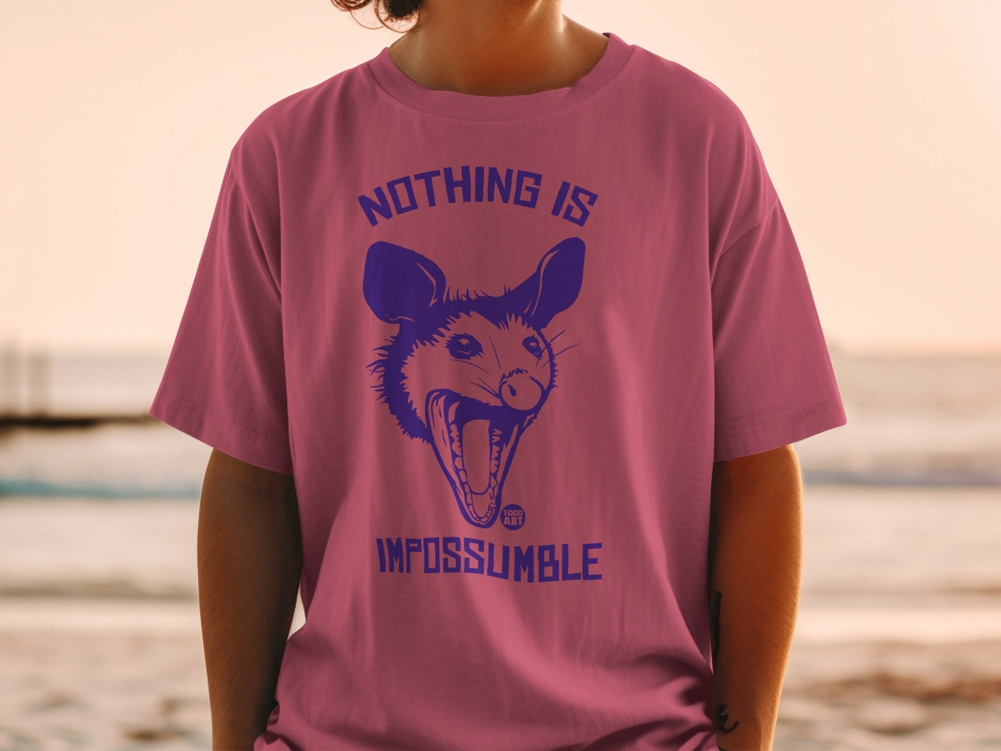 Pink t-shirt with blue graphic of an open-mouthed possum and text "NOTHING IS IMPOSSUMBLE".
