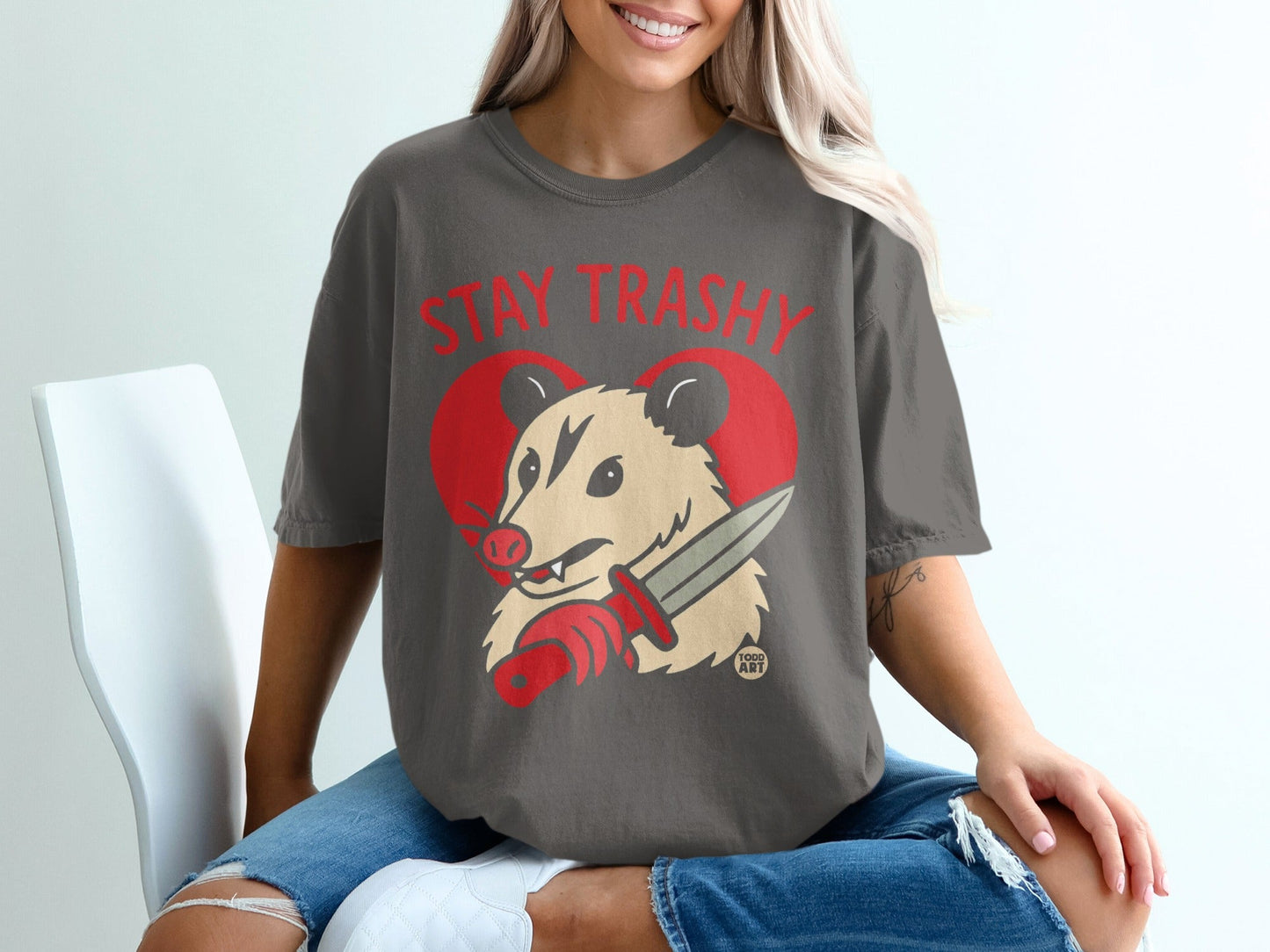 Opossum wearing a red heart tattoo, holding a knife, with "STAY TRASHY" text.