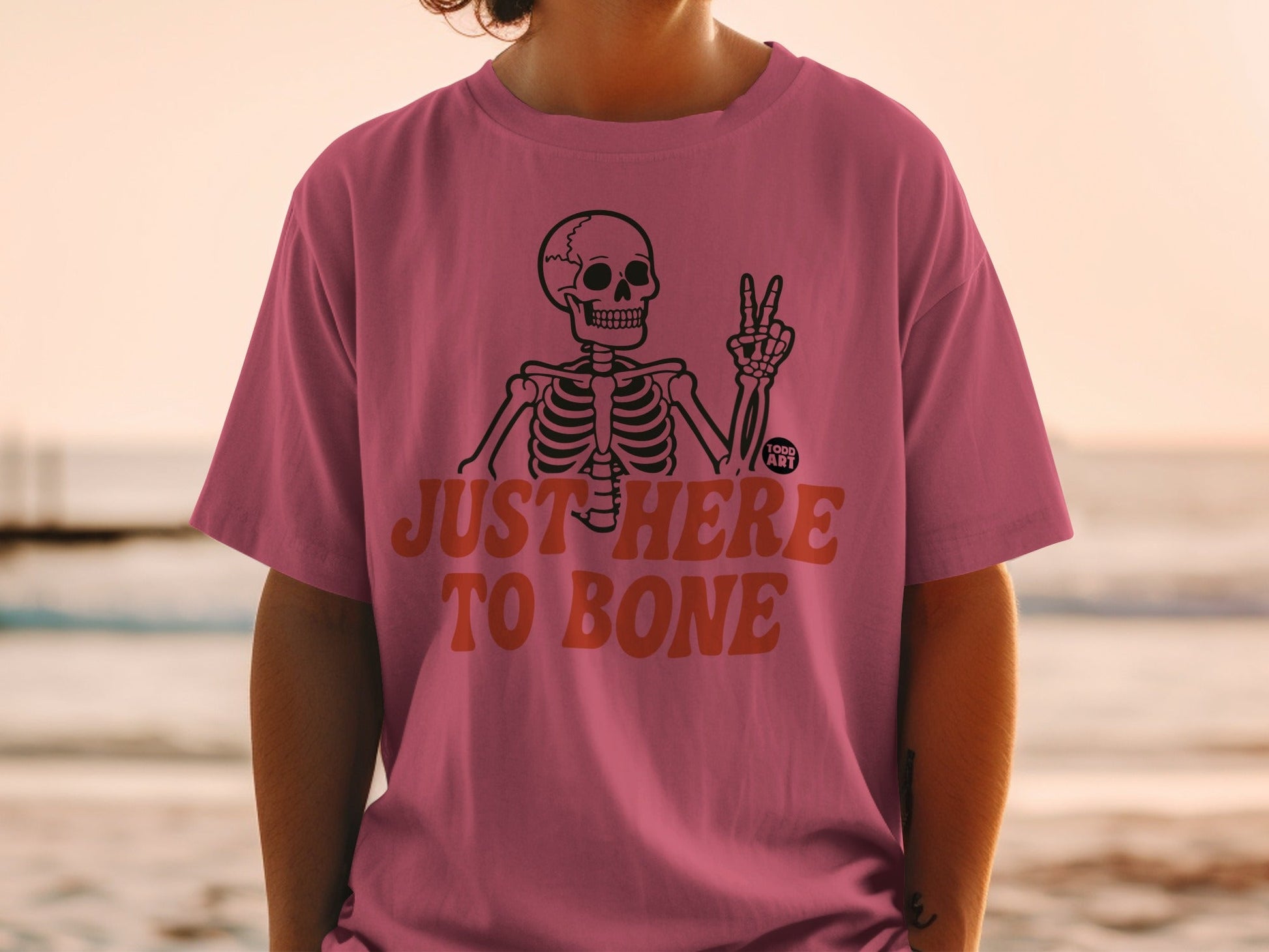 Pink t-shirt with skeleton graphic and "JUST HERE TO BONE" text.