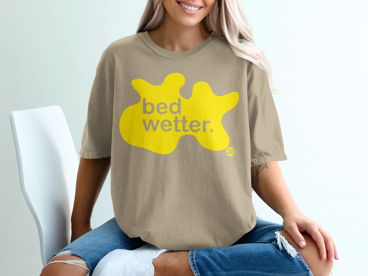 Tan t-shirt with yellow "bed wetter." graphic and small logo.