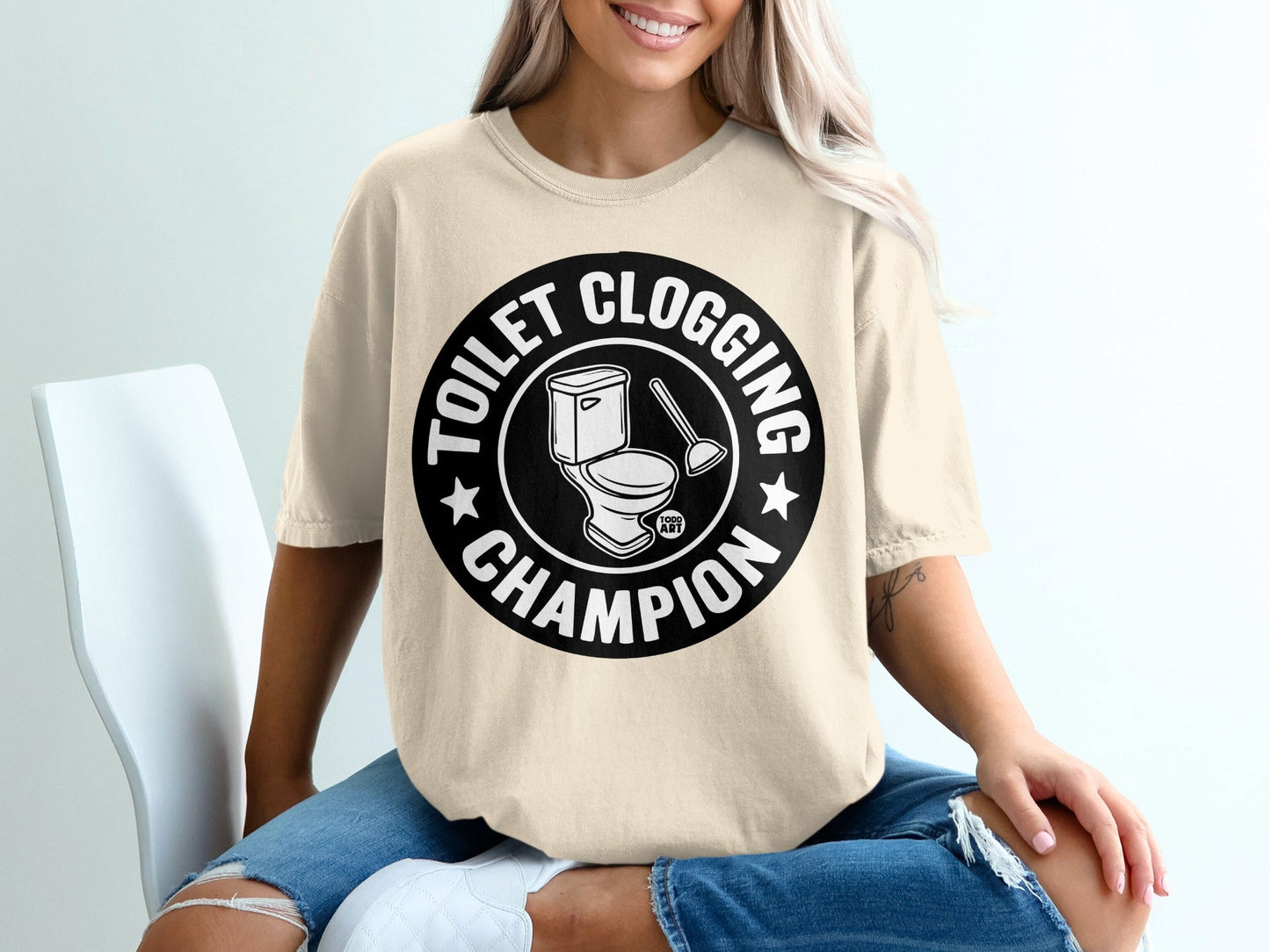 Cream t-shirt with "Toilet Clogging Champion" text and toilet plunger illustration.