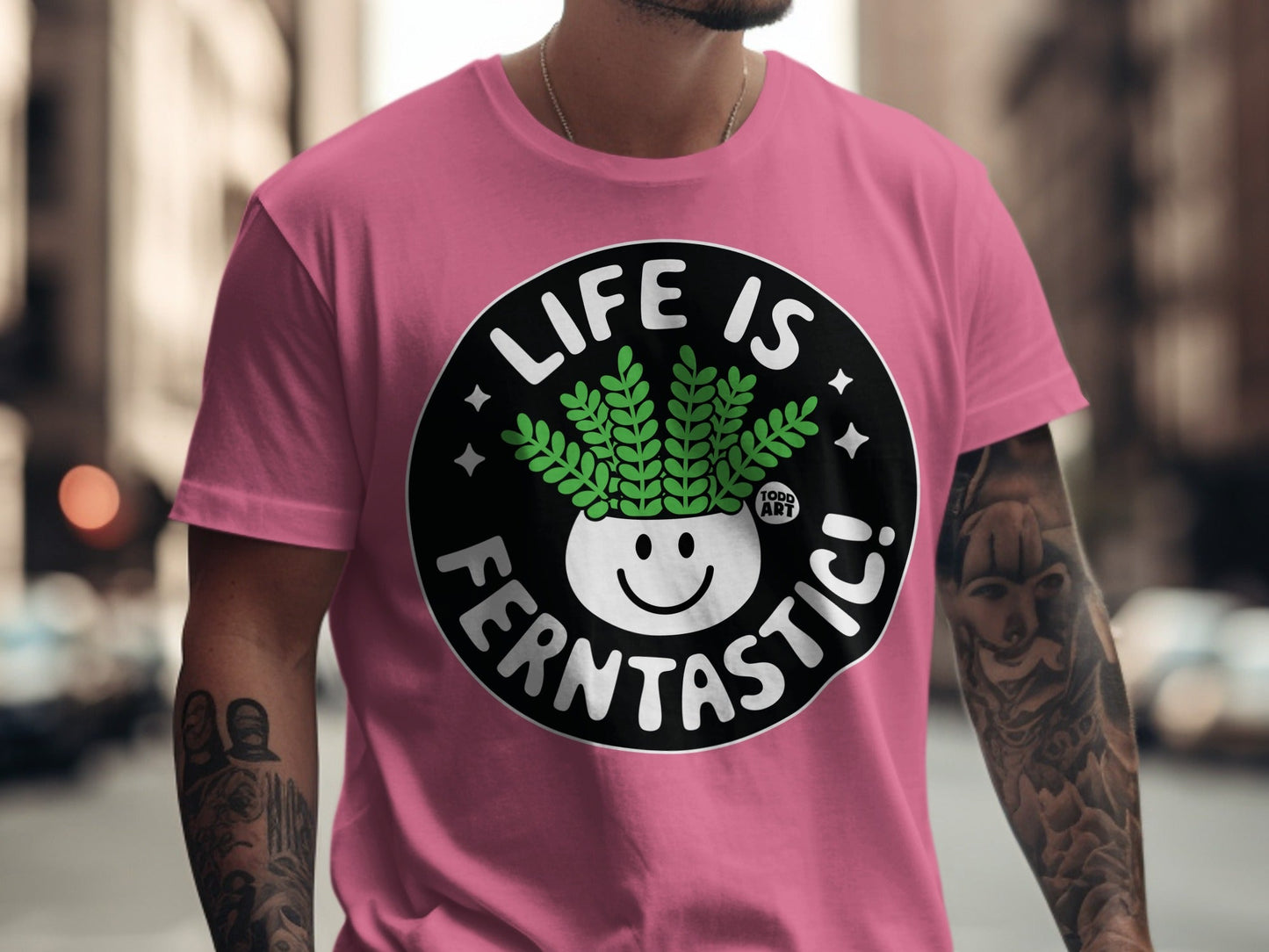 Pink t-shirt with a black circle graphic saying "LIFE IS FERN-TASTIC!" and a smiling potted fern.