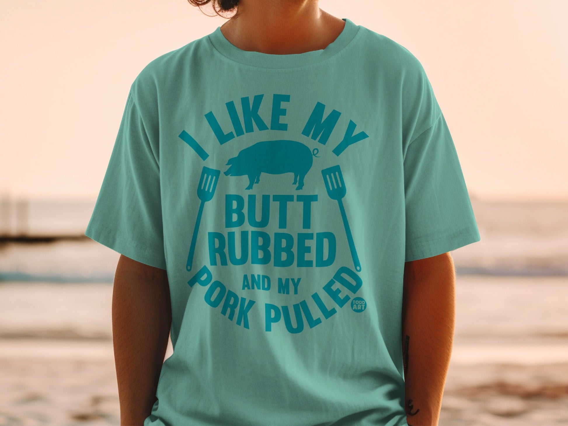 Teal t-shirt with "I Like My Butt Rubbed and Pork Pulled" graphic and pig silhouette.