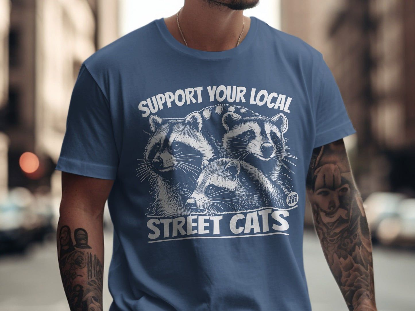 Blue t-shirt with "Support Your Local Street Cats" and raccoons graphic.