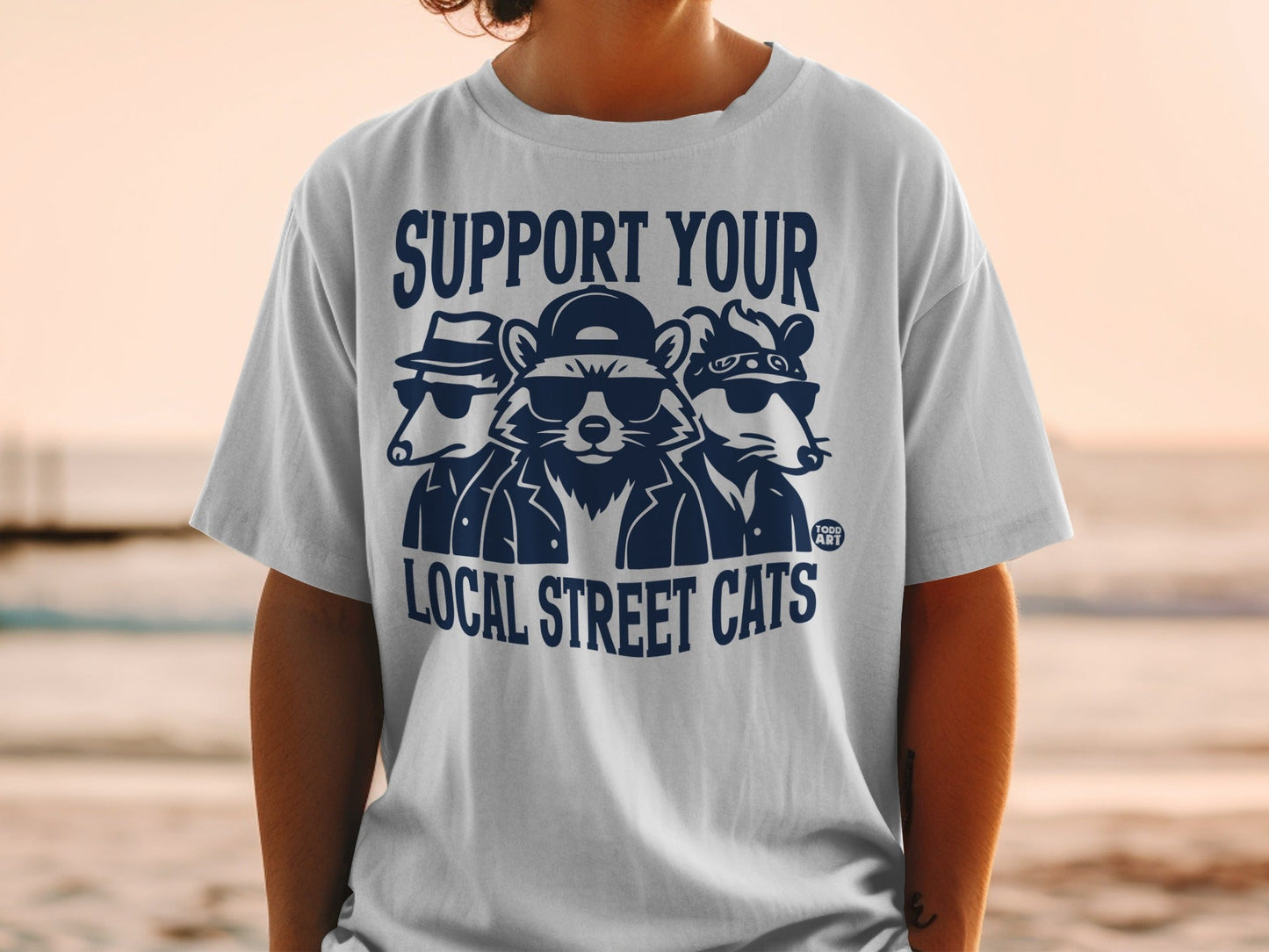 T-shirt graphic with three cartoon animals wearing sunglasses and hats, with text "SUPPORT YOUR LOCAL STREET CATS".