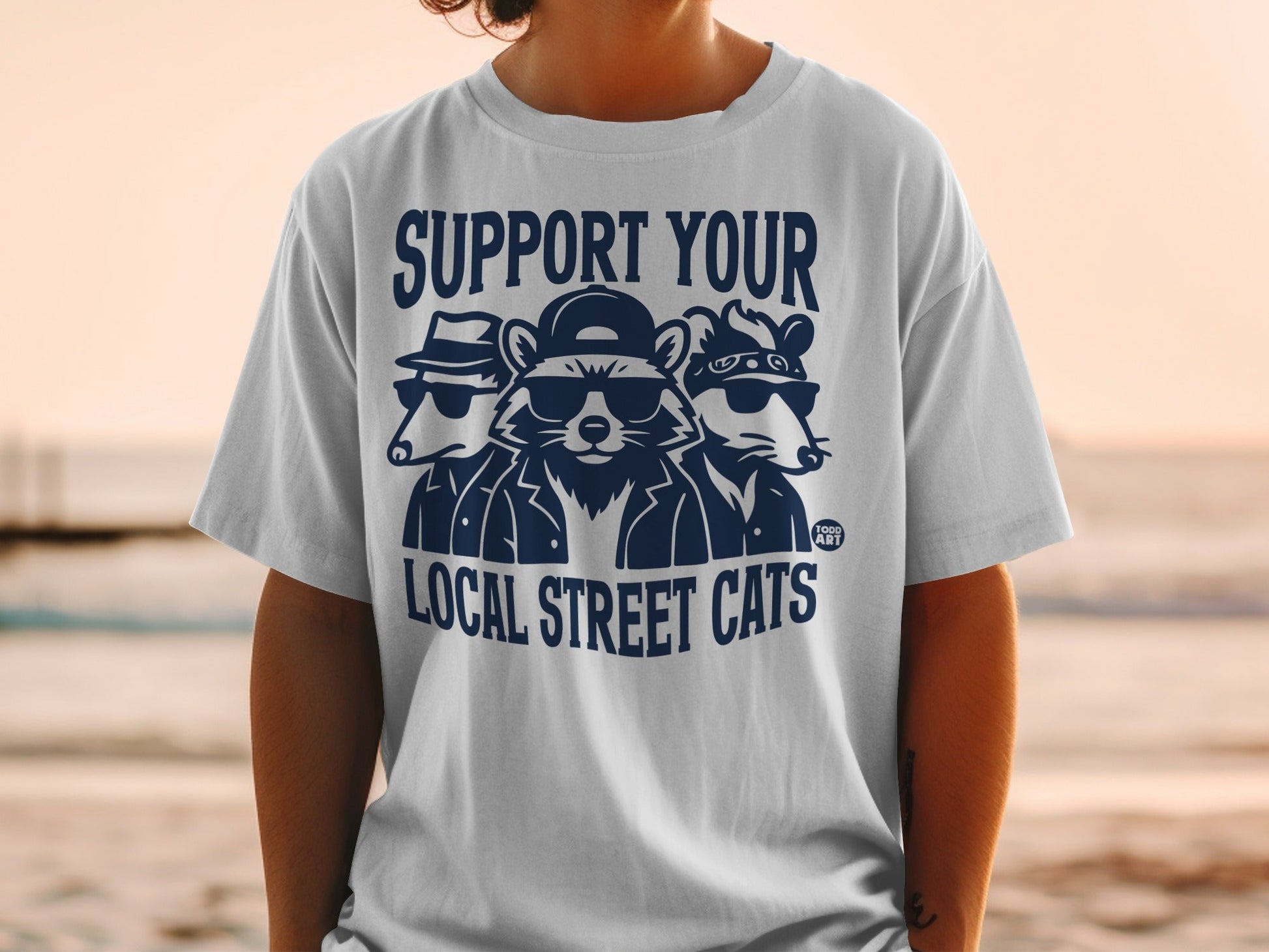 T-shirt graphic with three cartoon animals wearing sunglasses and hats, with text "SUPPORT YOUR LOCAL STREET CATS".