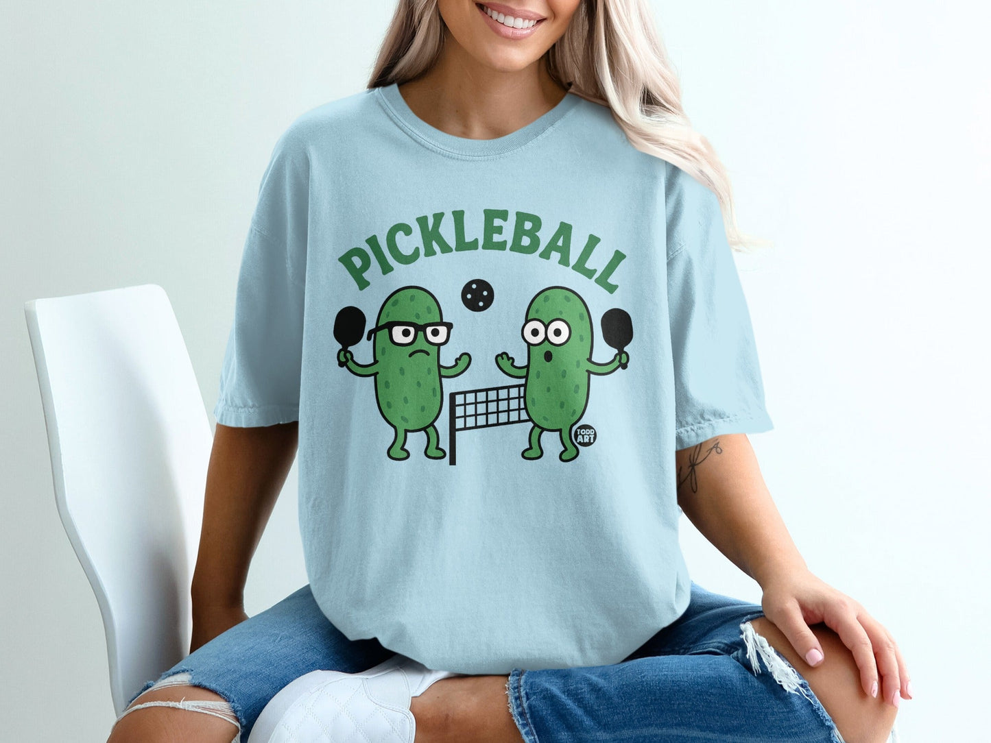 T-shirt with cartoon pickles playing pickleball, text "PICKLEBALL".