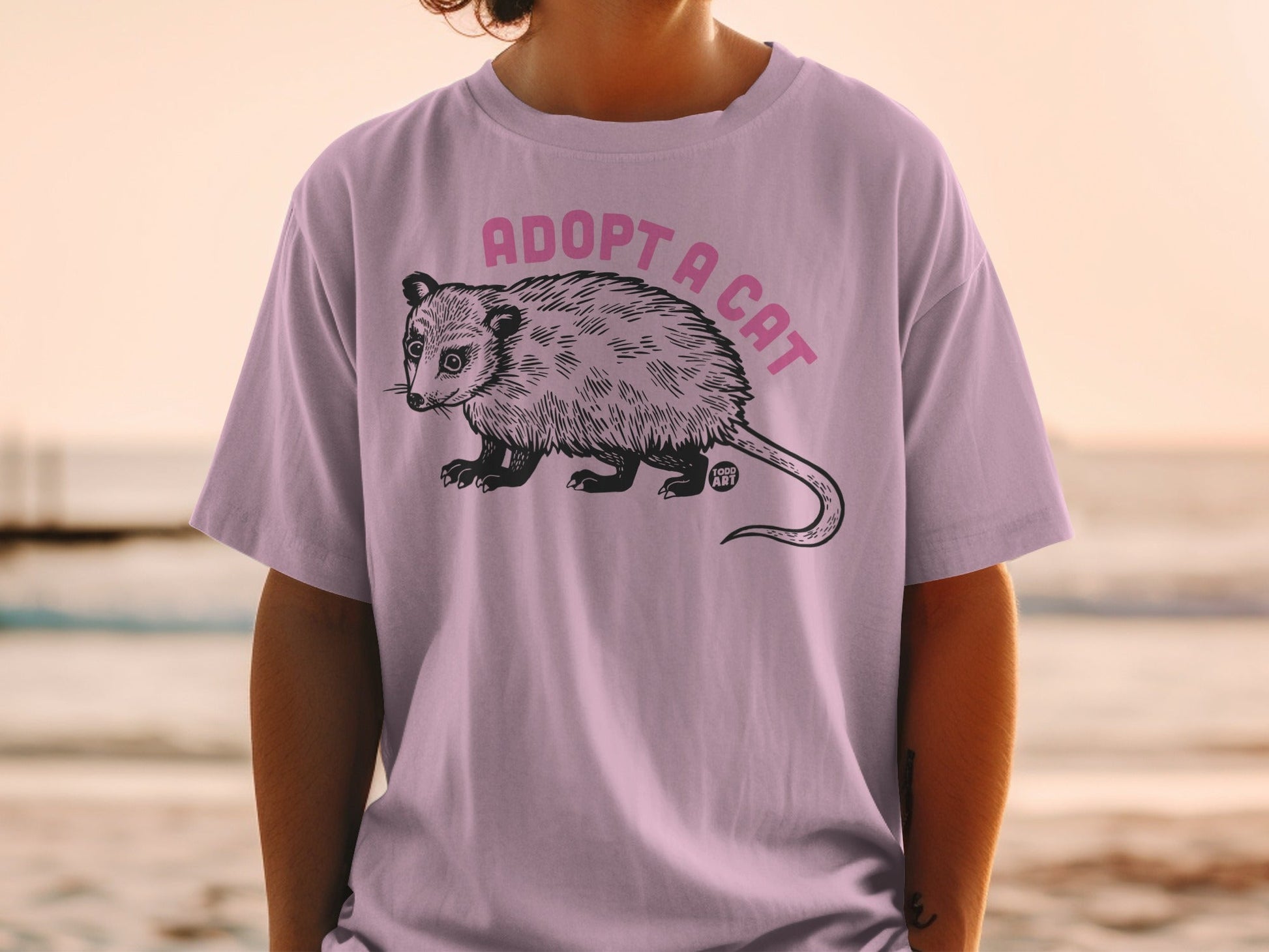 T-shirt with pink text "ADOPT A CAT" and opossum illustration.