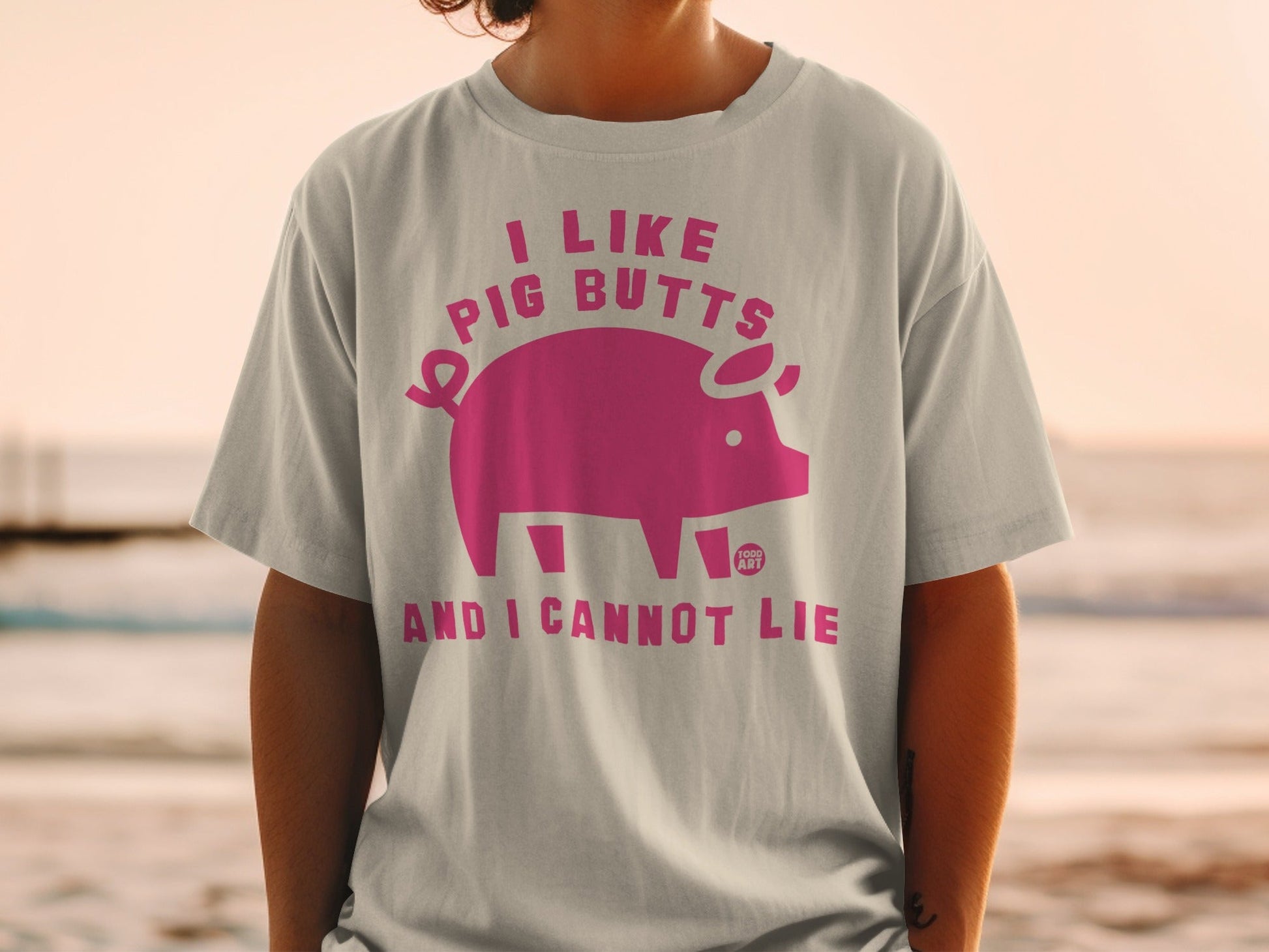 Cream t-shirt with pink text and pig graphic that reads "I like pig butts and I cannot lie."