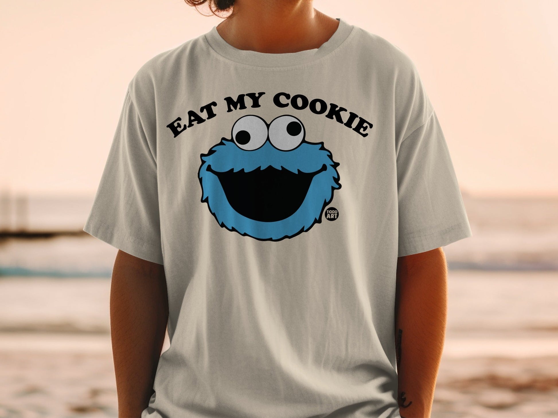 Cookie Monster graphic on light grey t-shirt, text "Eat My Cookie" above.
