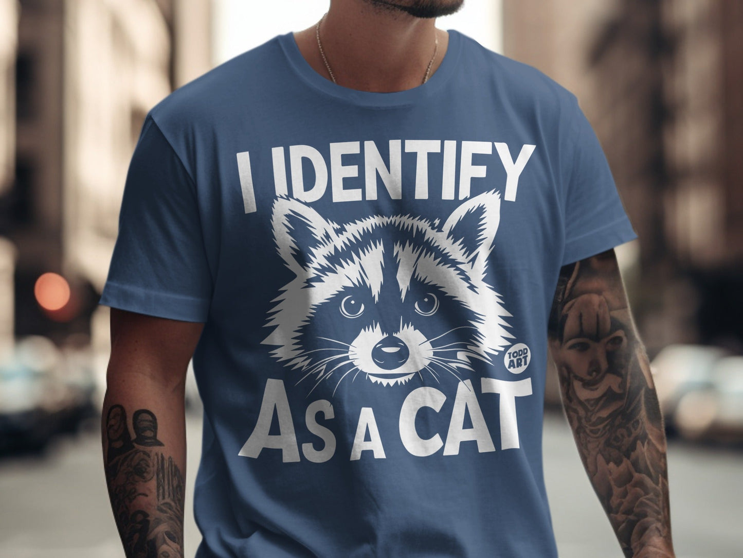 Blue t-shirt with a raccoon graphic and text "I IDENTIFY AS A CAT".
