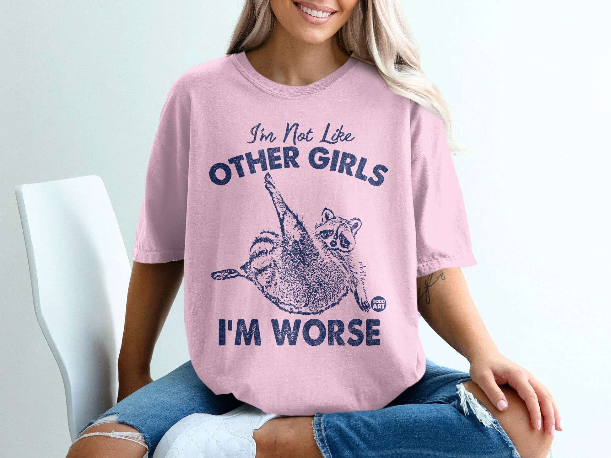 Pink t-shirt with navy text and a raccoon graphic, "I'M NOT LIKE OTHER GIRLS I'M WORSE".