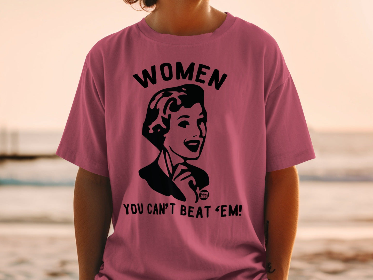 Pink t-shirt with black graphic that reads "WOMEN YOU CAN'T BEAT 'EM!"