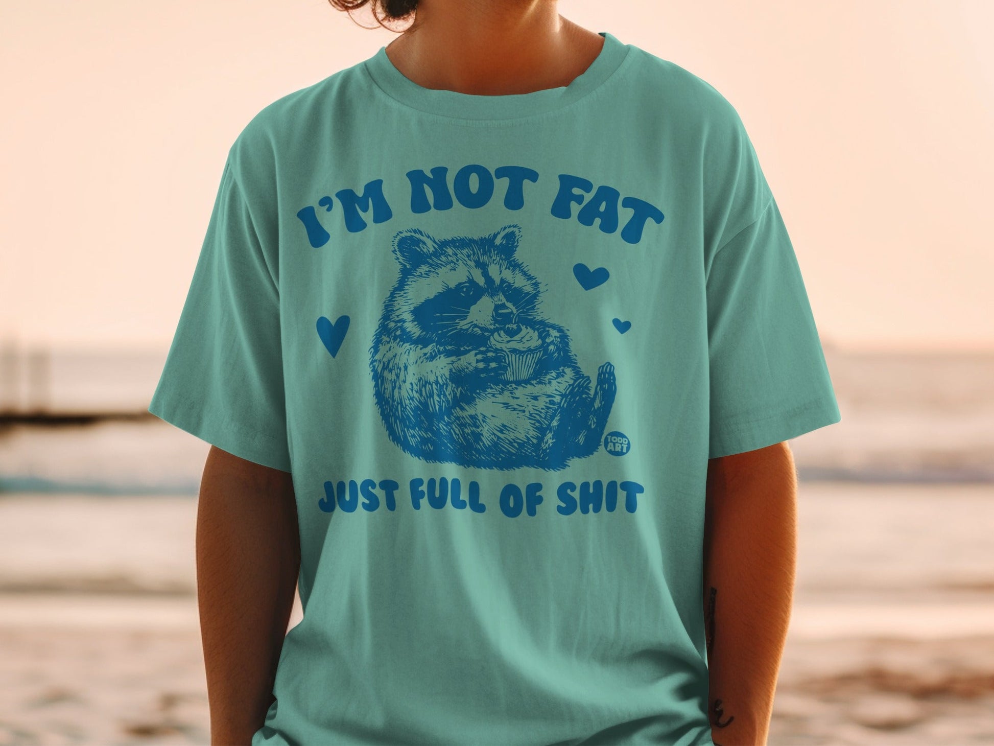 Teal t-shirt with raccoon graphic and text "I'M NOT FAT JUST FULL OF SHIT".