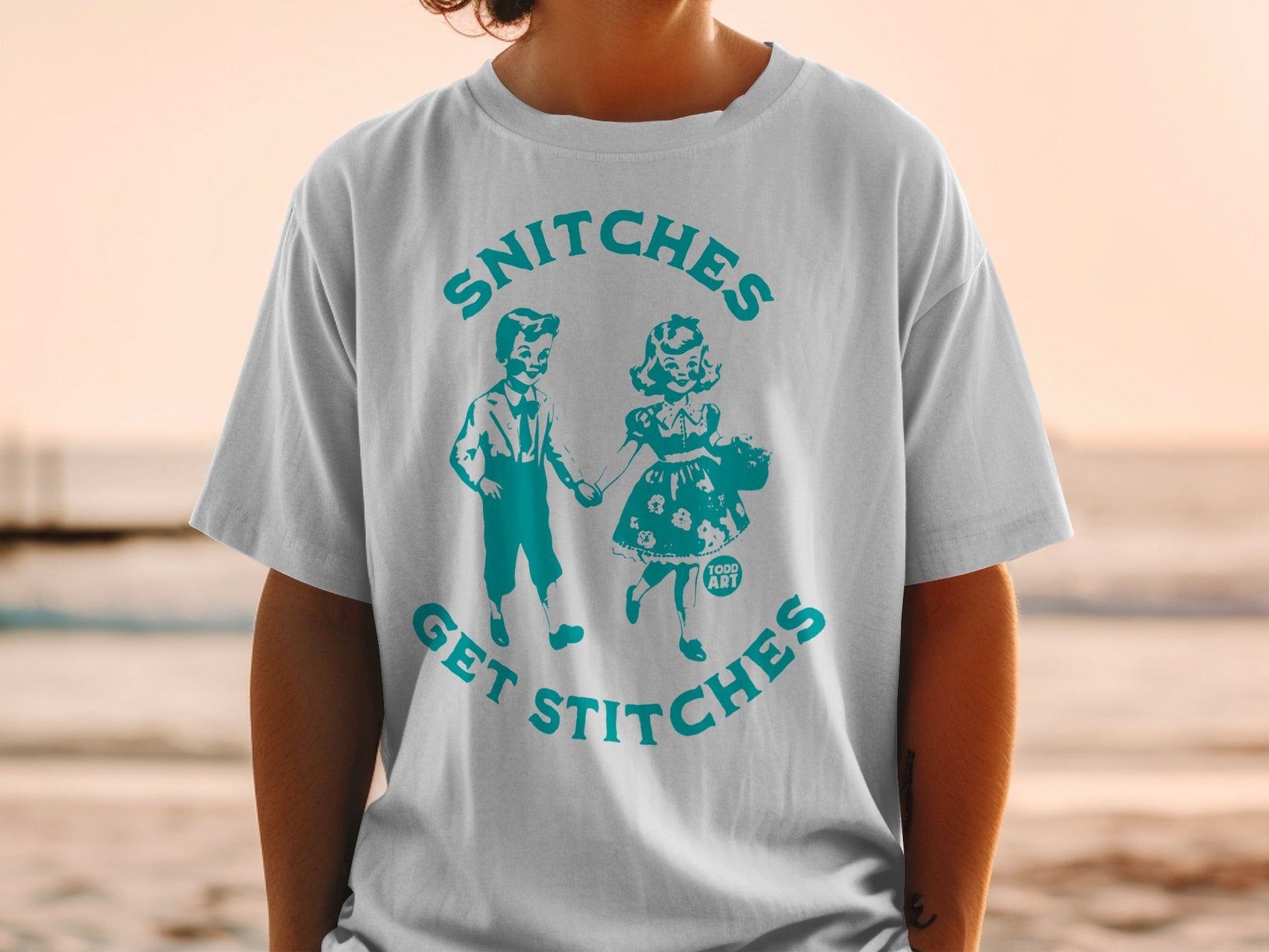 T-shirt with "Snitches Get Stitches" text and a vintage illustration of two children.