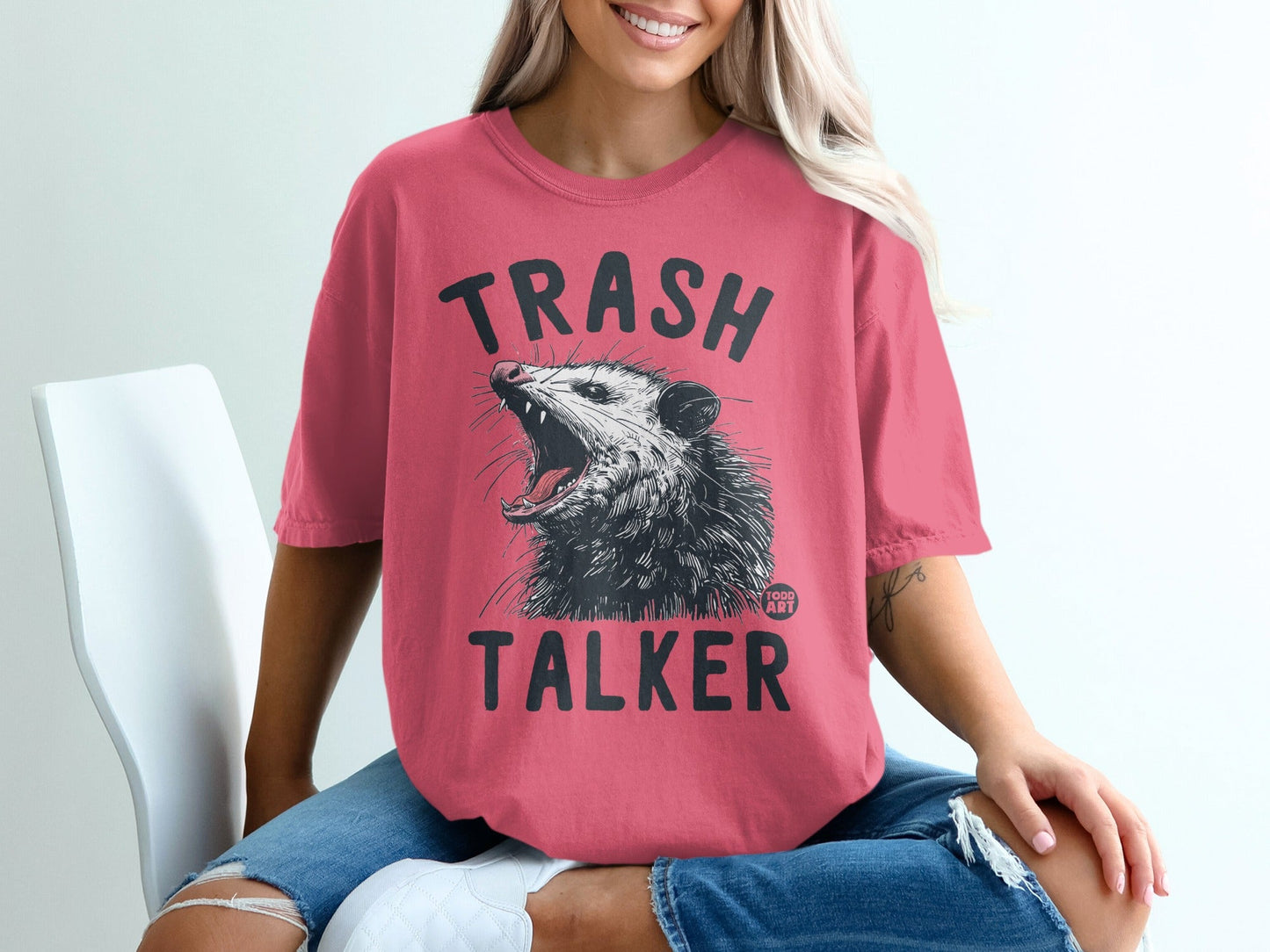 Pink t-shirt with a black graphic of a snarling opossum and text reading "TRASH TALKER".