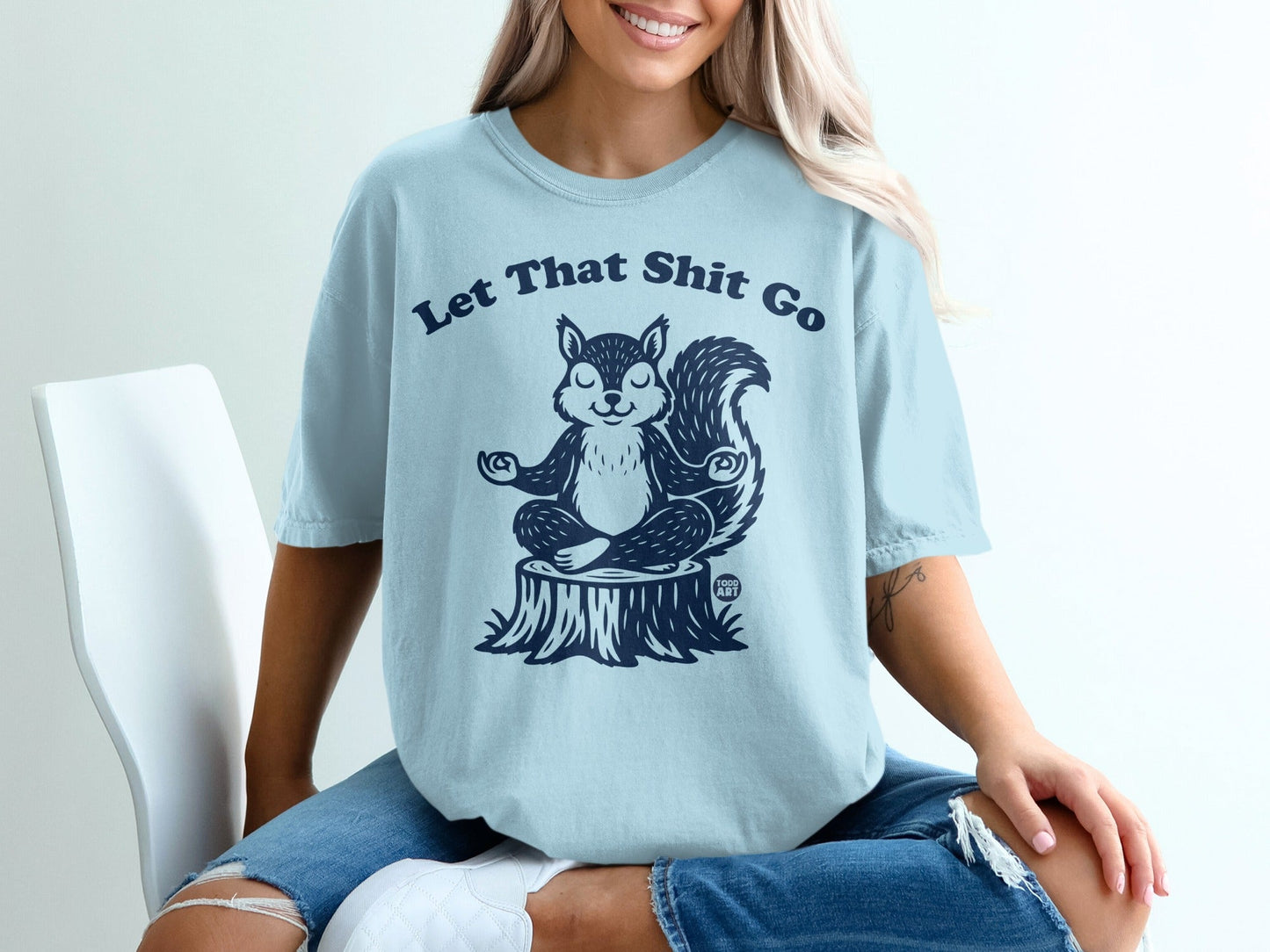 Light blue t-shirt with a meditating squirrel on a tree stump, text "Let That Shit Go".