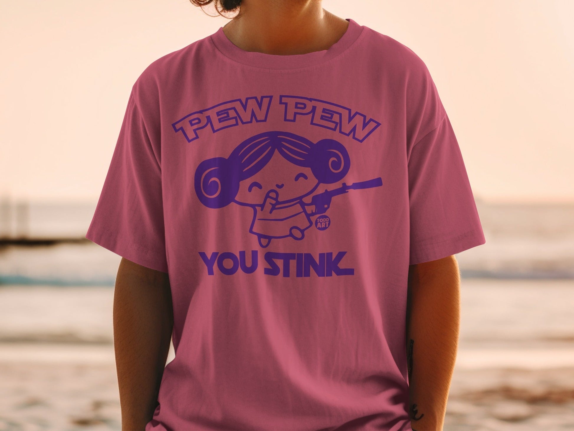 Pink t-shirt with purple cartoon girl holding a gun, "Pew Pew You Stink" text.