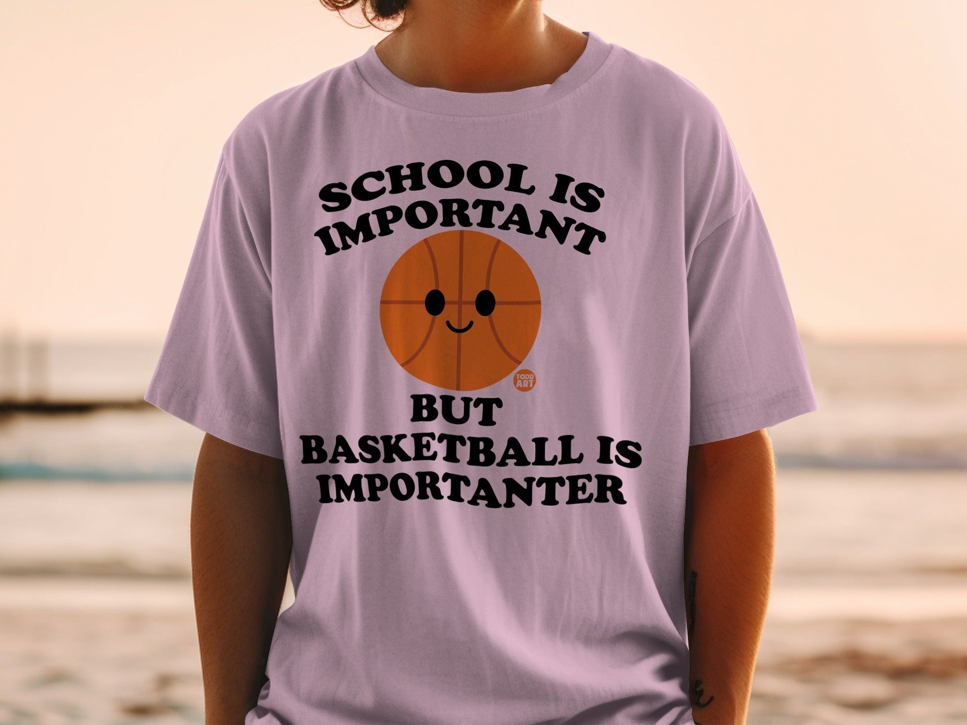 Lilac t-shirt with a basketball and text reading "SCHOOL IS IMPORTANT BUT BASKETBALL IS IMPORTANTER".