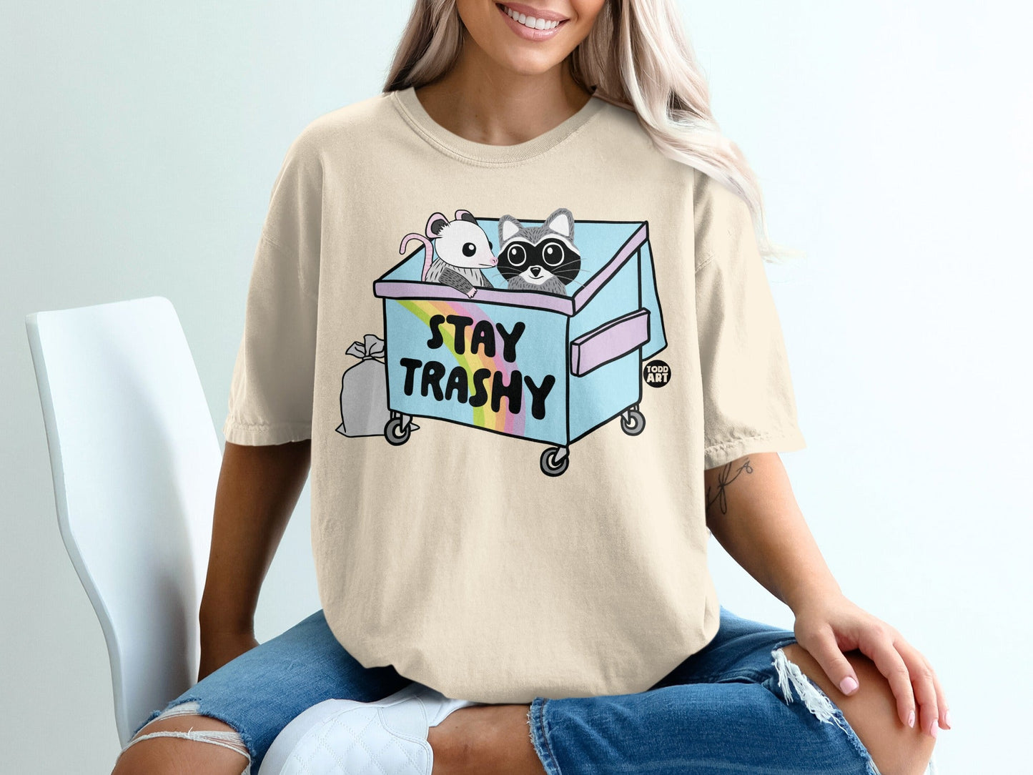Light beige t-shirt with cartoon raccoon and mouse in a trash can.